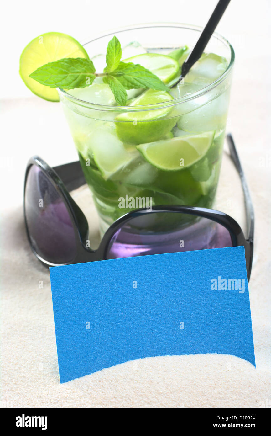 Blank blue card on sand with sunglasses and a mojito cocktail in the back (Selective Focus, Focus on the card) Stock Photo