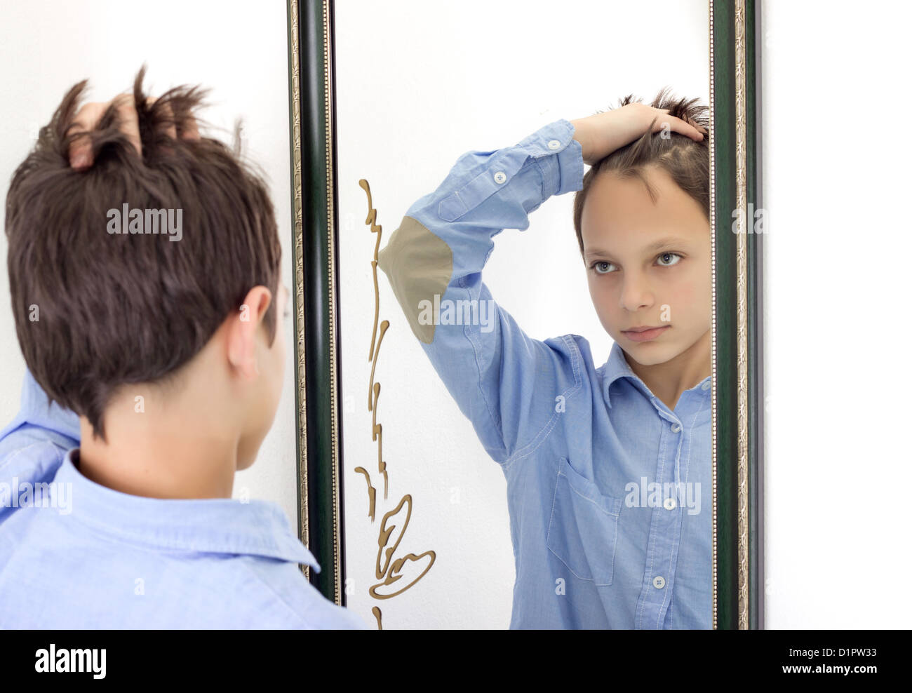 horizontal photograph of a young boy combing his hair while looking at himself in a mirror Stock Photo