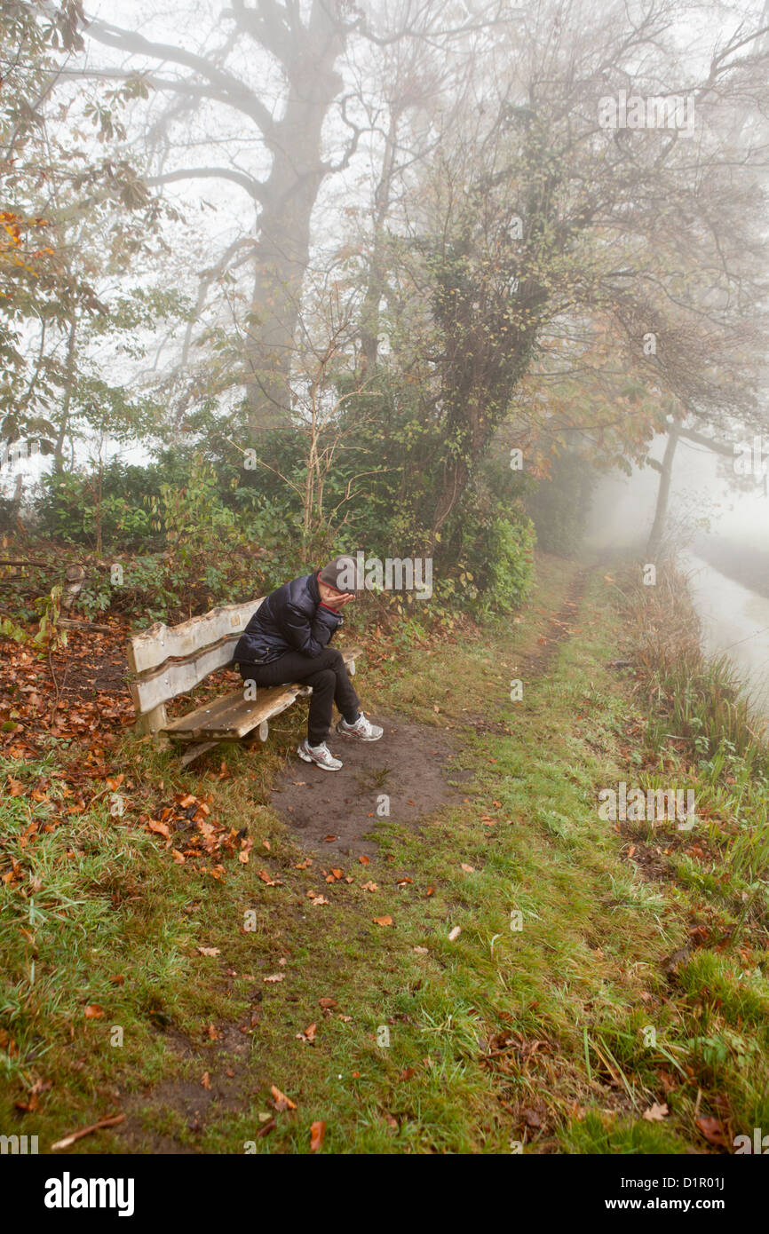 The Netherlands, 's-Graveland, Woman sitting on bench with hands in front of her face. Stock Photo