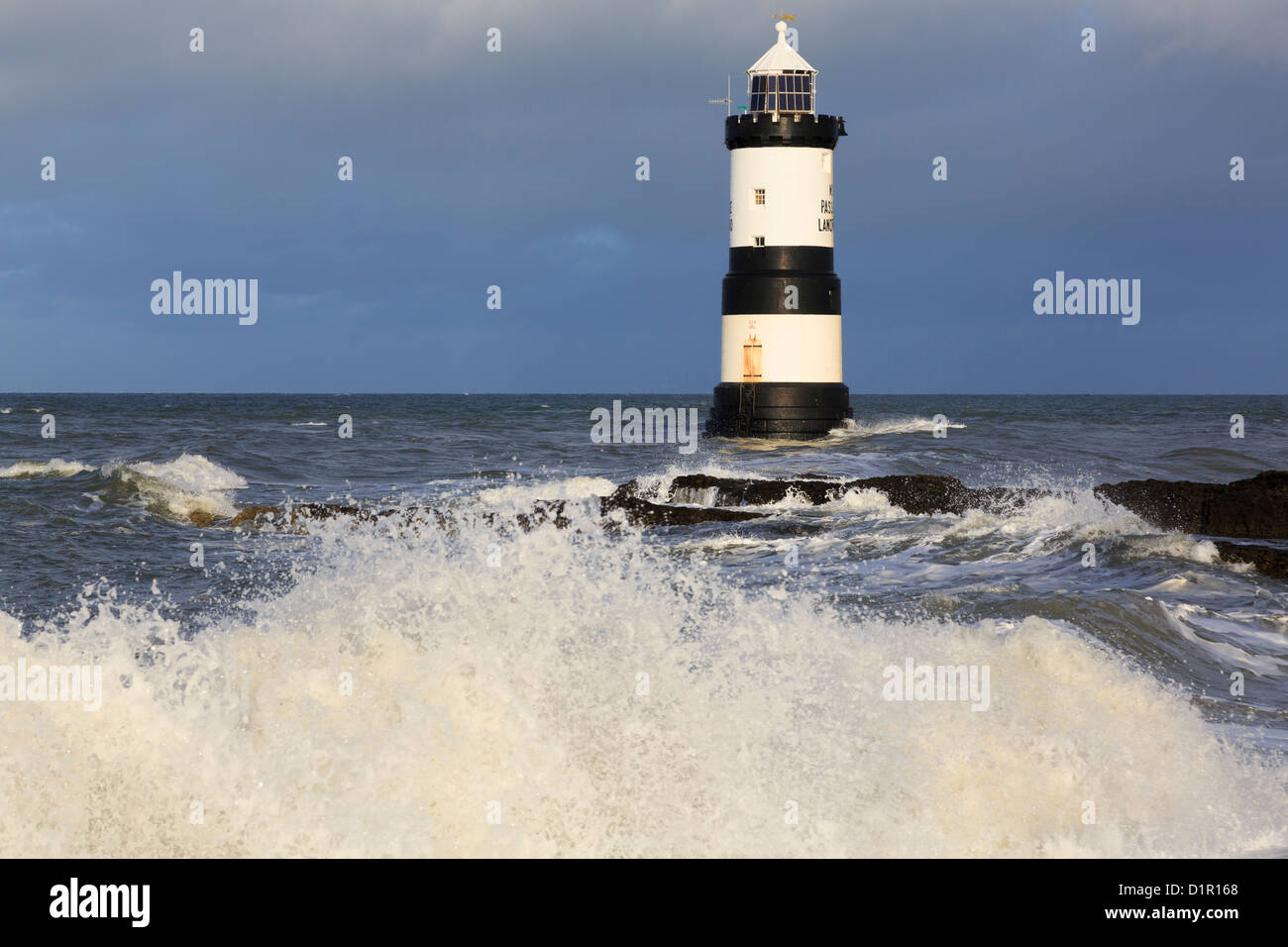 Large waves crashing onshore with black and white Penmon lighthouse (Trwyn Du) offshore on wild coast at Penmon Point Isle of Anglesey North Wales UK Stock Photo