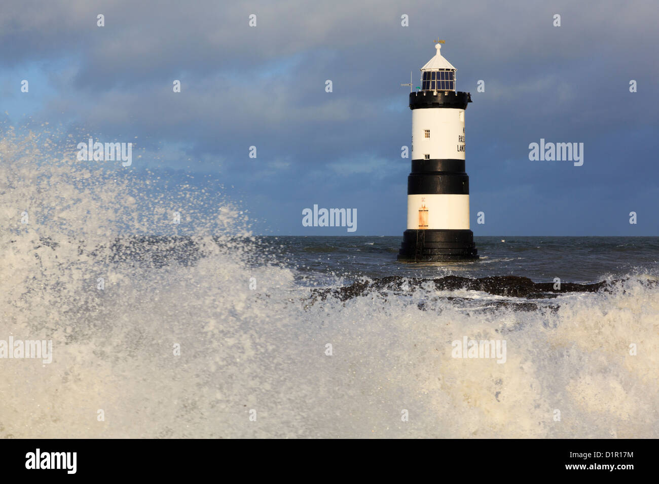 Large waves crashing onshore with black and white Penmon lighthouse (Trwyn Du) offshore at Penmon Point Isle of Anglesey North Wales UK Britain Stock Photo