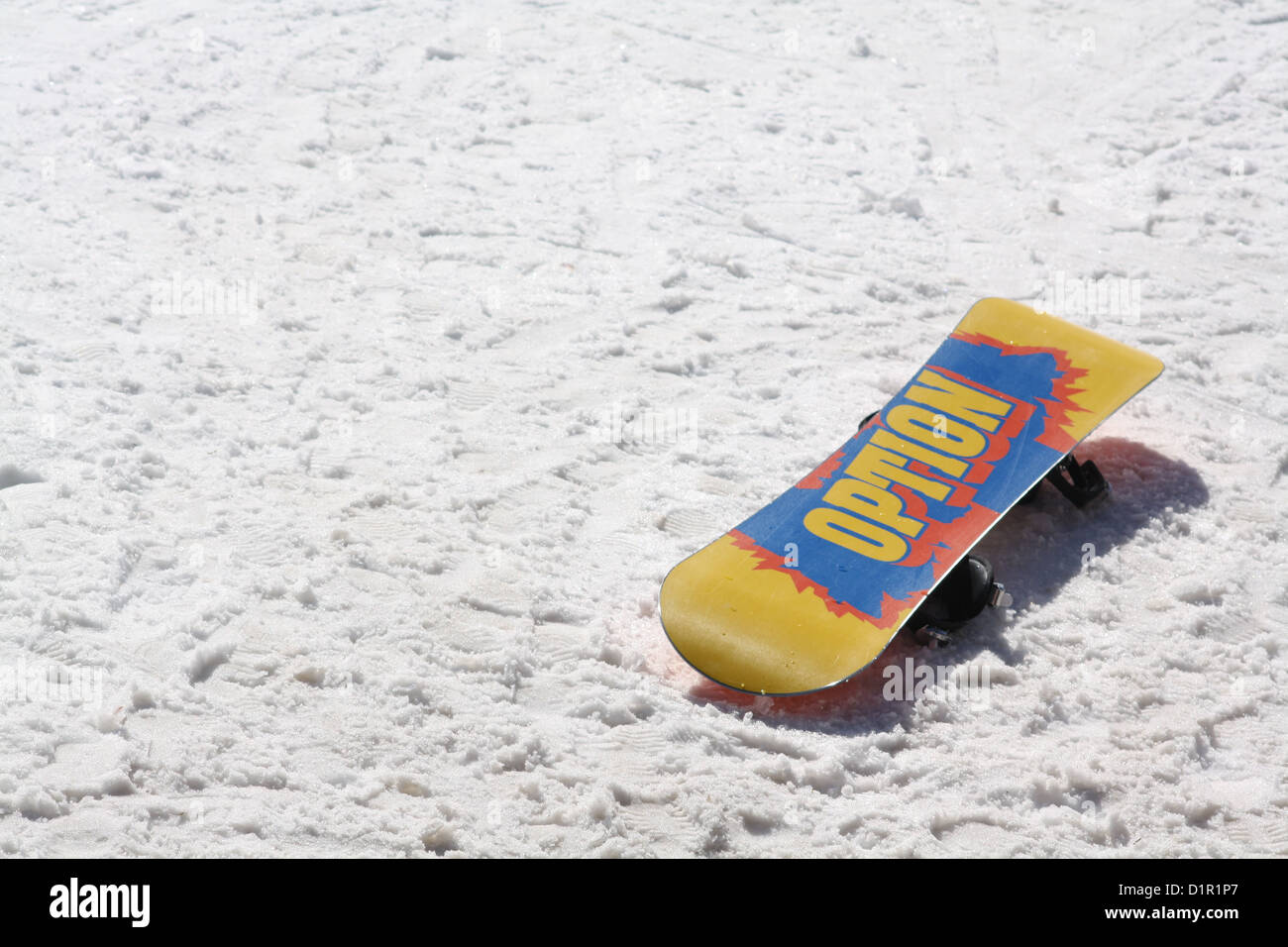 Canary yellow snowboard lies upside down in snow revealing large blue and red Option logo on the underside Stock Photo