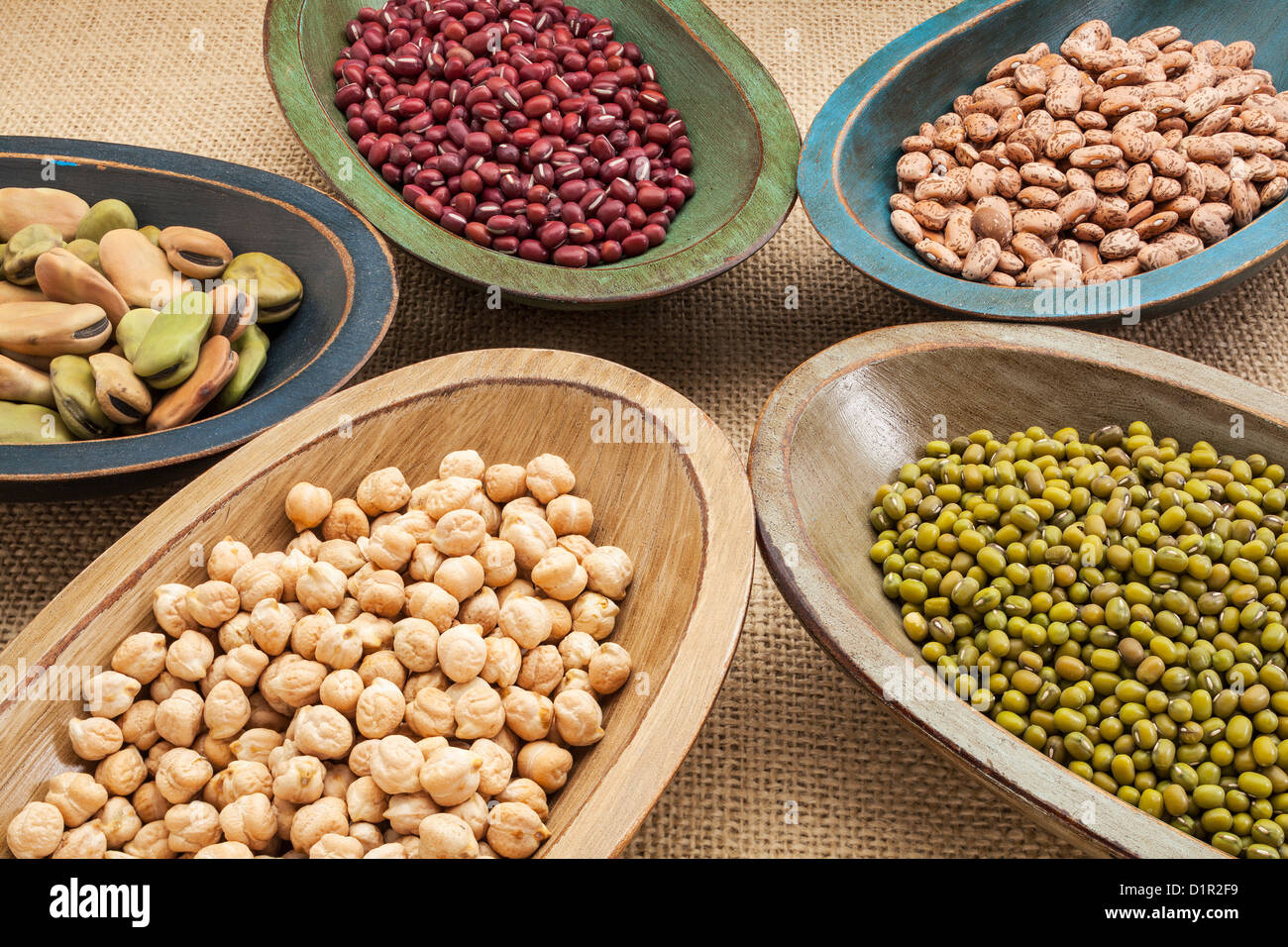 variety of legumes (fava bean, mung bean, adzuki, pinto, chickpea) in colorful rustic wood bowls on canvas Stock Photo