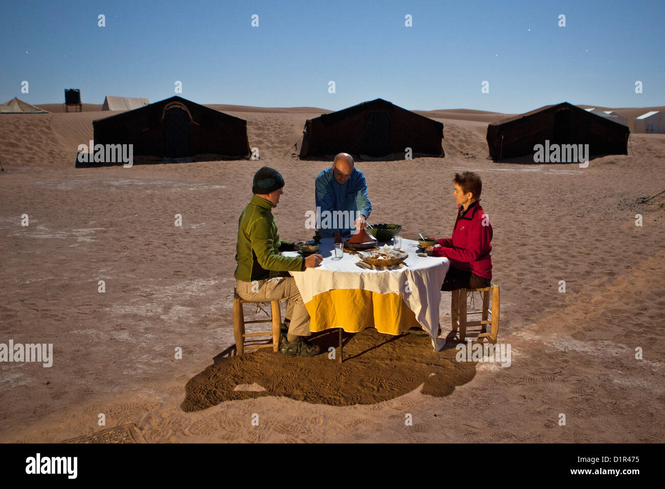 Morocco, M'Hamid, Erg Chigaga sand dunes. Sahara desert. Tourist camp, bivouac. Tourists having dinner at full moon light. Stock Photo