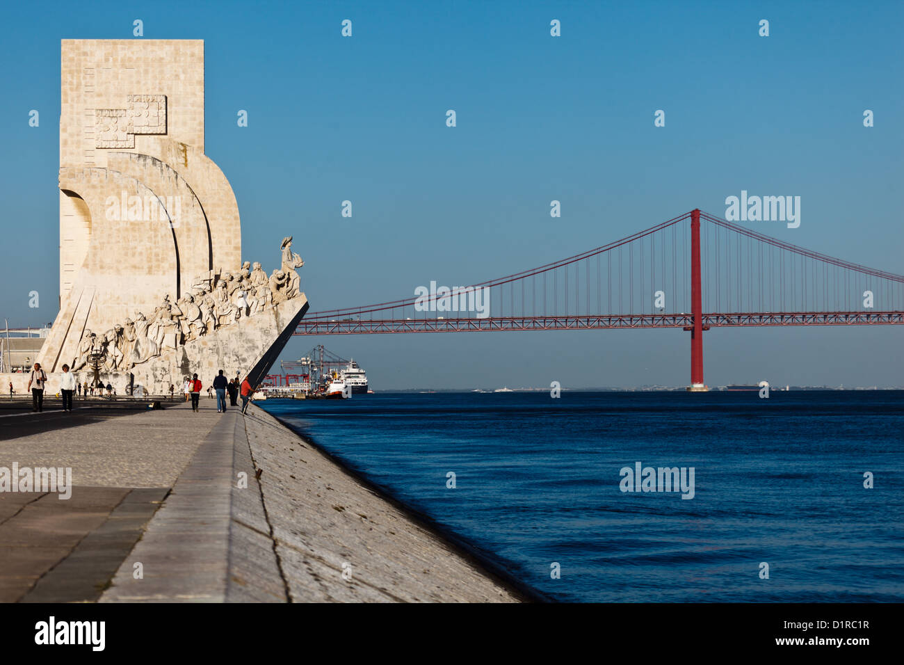 Wharf at harbor entrance with Monument to Discoveries and Lisbon's 25th of April Bridge crossing the Tagus river Stock Photo