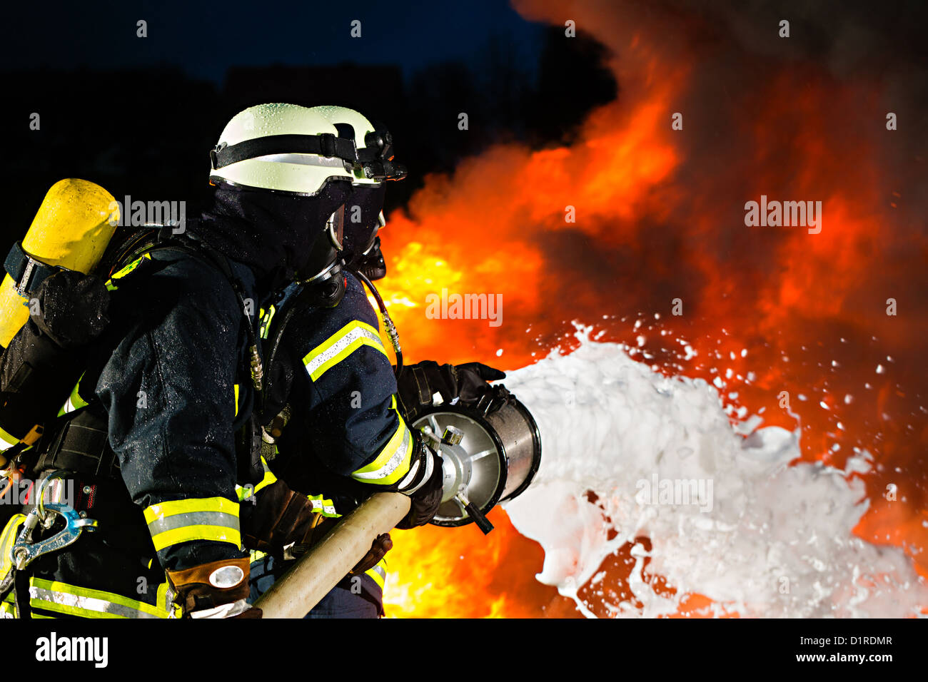 Firefighter - Firemen extinguishing a large blaze, they are standing with protective wear in front of wall of fire Stock Photo