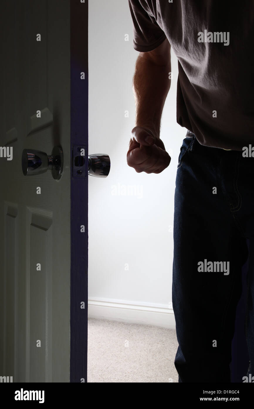 Aggressive male entering a dark room, fist clenched. Face not shown. Stock Photo