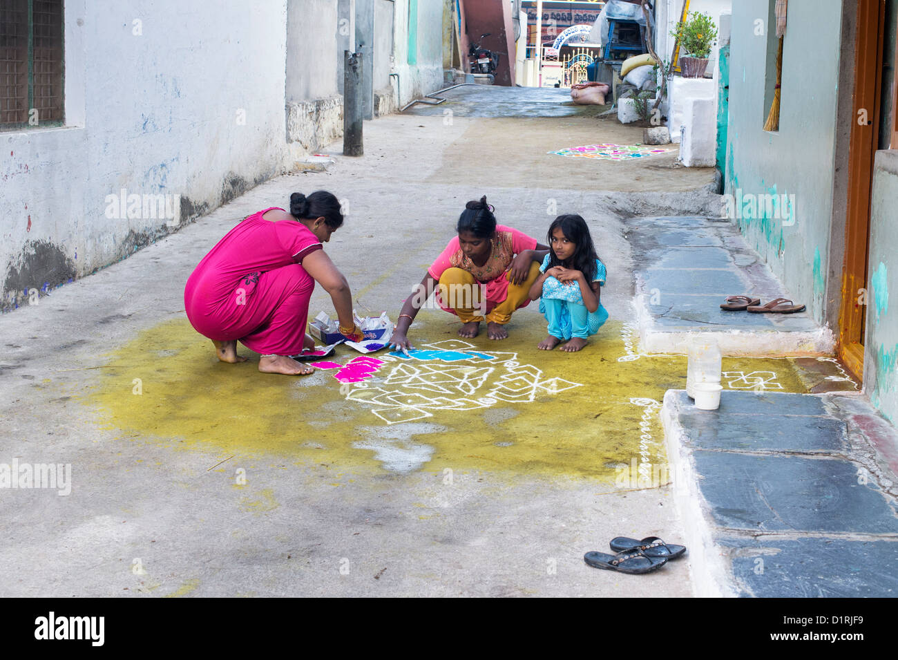 Indian mother and daughters making a Rangoli festival design outside their home during the festival of sankranthi. Puttaparthi, Andhra Pradesh, India Stock Photo