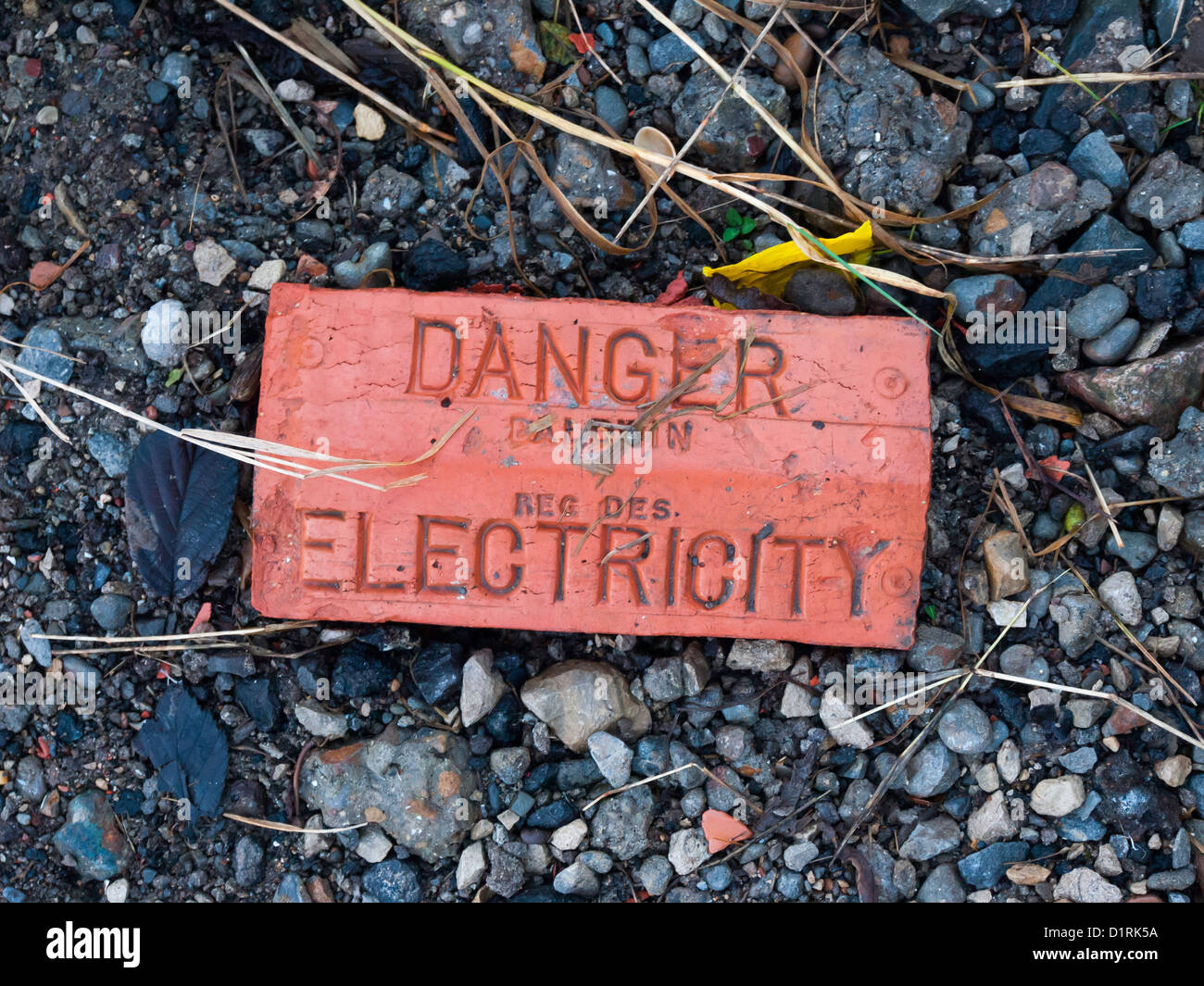 Brick tile labeled Danger Electricity. These used to be laid over cables in the ground, now often replaced by plastic tape Stock Photo