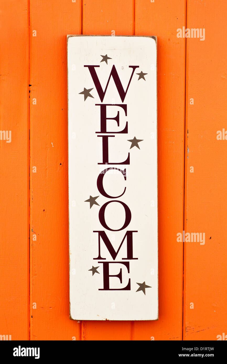 A folksy styled wooden 'Welcome' sign on the side of a brightly colored wooden building. Stock Photo