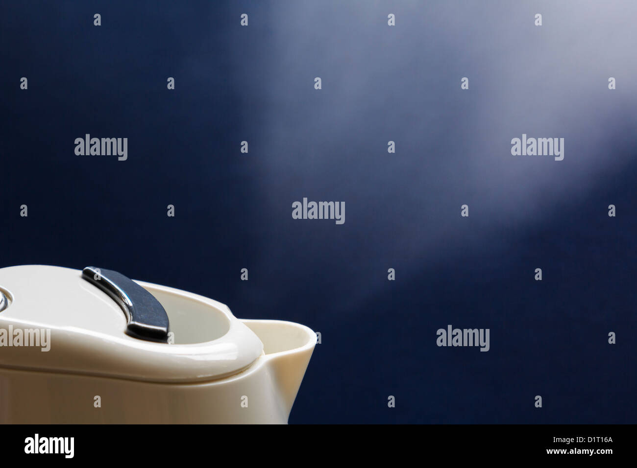 Modern electric kettle boiling water and steaming from the spout showing clear gap as gas condenses against a dark background Stock Photo