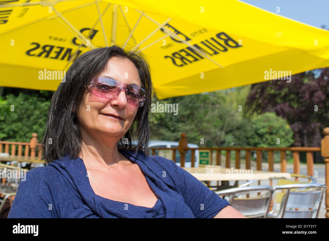 British Indian Woman Sitting under Yellow Sunshade Outside Country Pub Stock Photo
