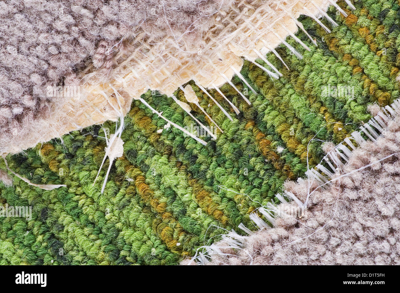 background detail of old ripped tan carpet over green carpet Stock Photo