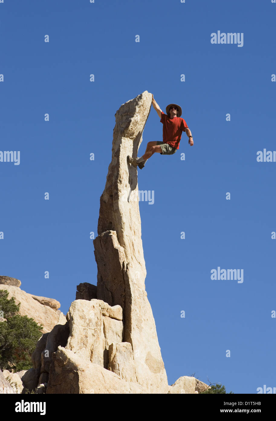a man climbing up a steep narrow rock spire Stock Photo