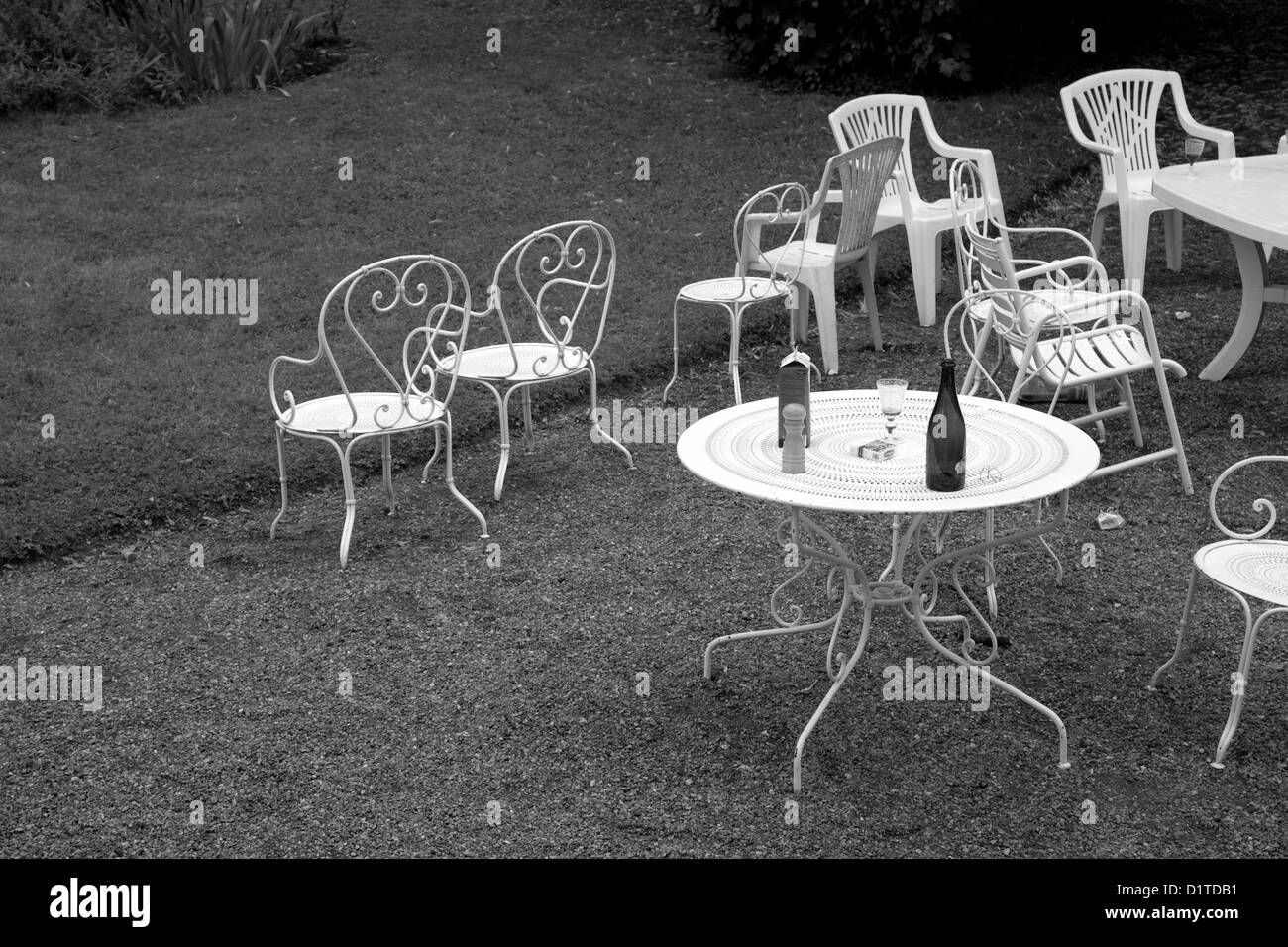 Black and white image of white outdoor chairs and a table after a party in a garden in France. Stock Photo