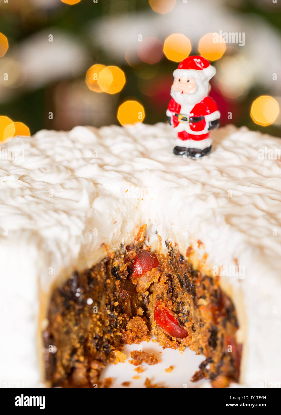 Slice out of iced Christmas cake with lights of xmas tree out of focus in background Stock Photo
