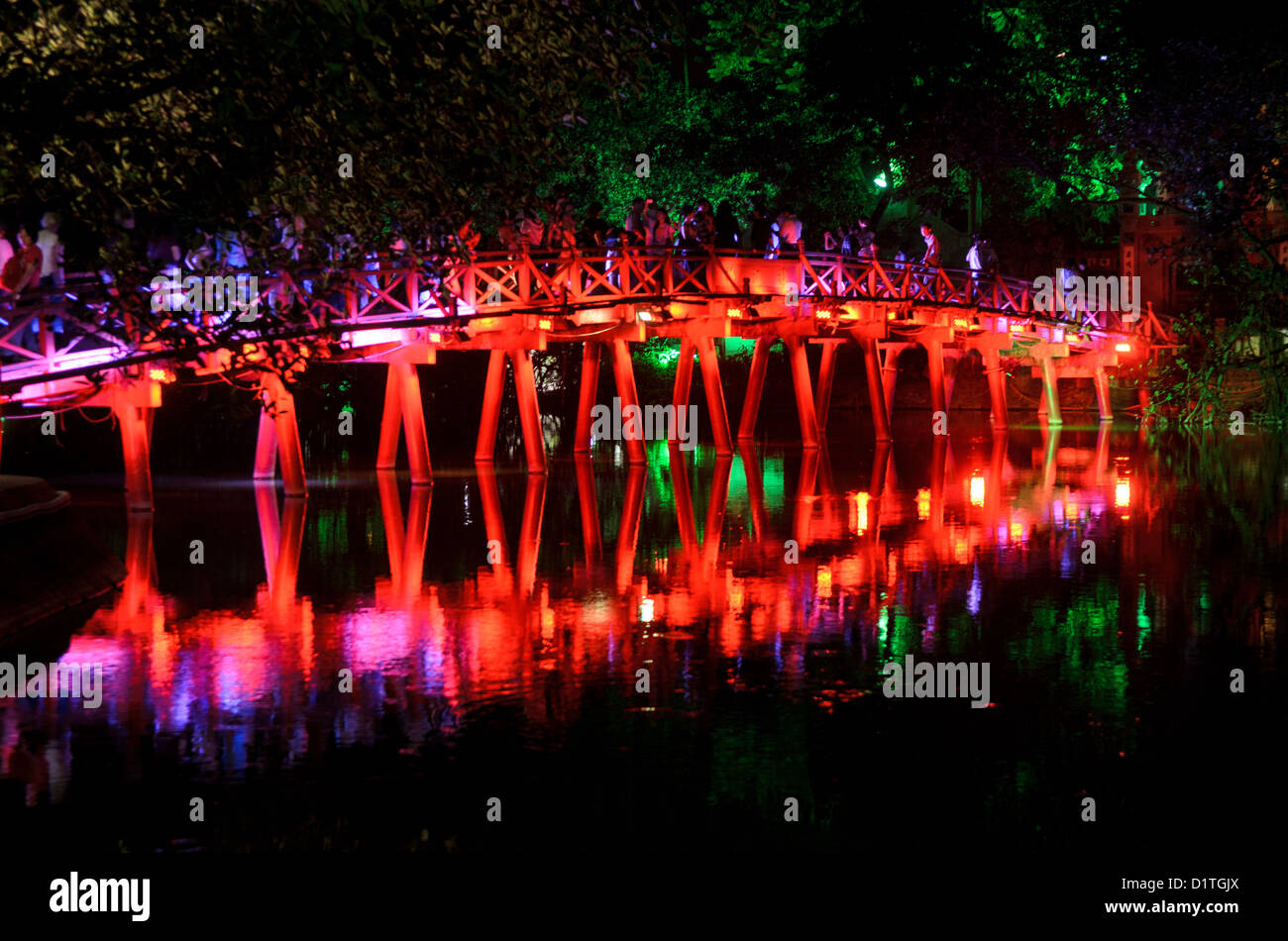 Huc Bridge At Night Hanoi Vietnam // HANOI, Vietnam — The Huc Bridge (Morning Sunlight Bridge) at night. The red-painted, wooden bridge joins the northern shore of the lake with Jade Island and the Temple of the Jade Mountain (Ngoc Son Temple). Stock Photo