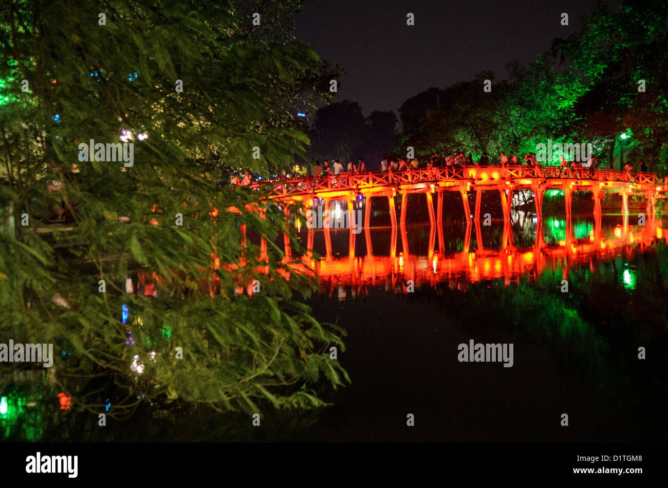 The Huc Bridge At Night Hanoi Vietnam // HANOI, Vietnam — Many tourists visit the The Huc Bridge (Morning Sunlight Bridge) at night. The red-painted, wooden bridge joins the northern shore of the lake with Jade Island and the Temple of the Jade Mountain (Ngoc Son Temple). Stock Photo