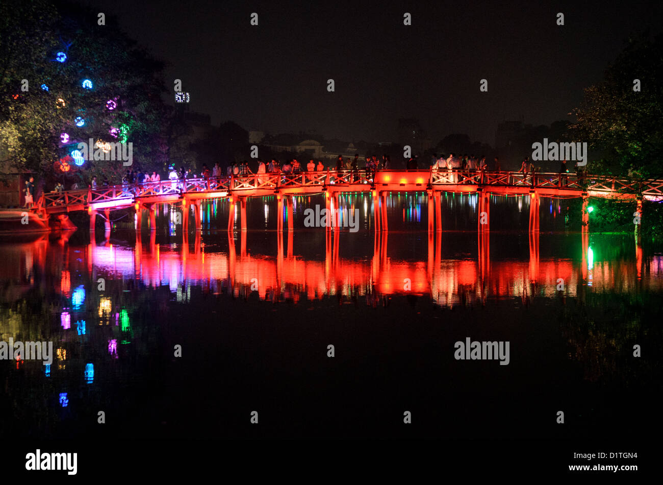 The Huc Bridge Hoan Kiem Lake Hanoi Vietnam // HANOI, Vietnam — View of The Huc Bridge (Morning Sunlight Bridge) from the northern shore of Hoan Kiem Lake at night. The red-painted, wooden bridge joins the northern shore of the lake with Jade Island and the Temple of the Jade Mountain (Ngoc Son Temple). Stock Photo