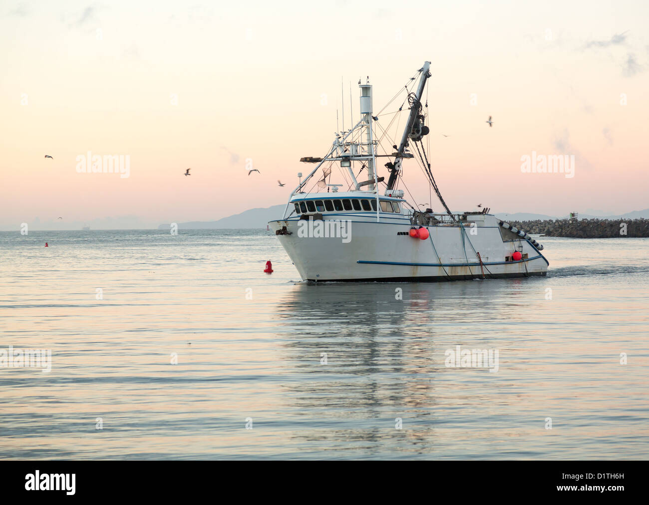 Fishing boat trawler entering harbor at Ventura at dawn with lights and