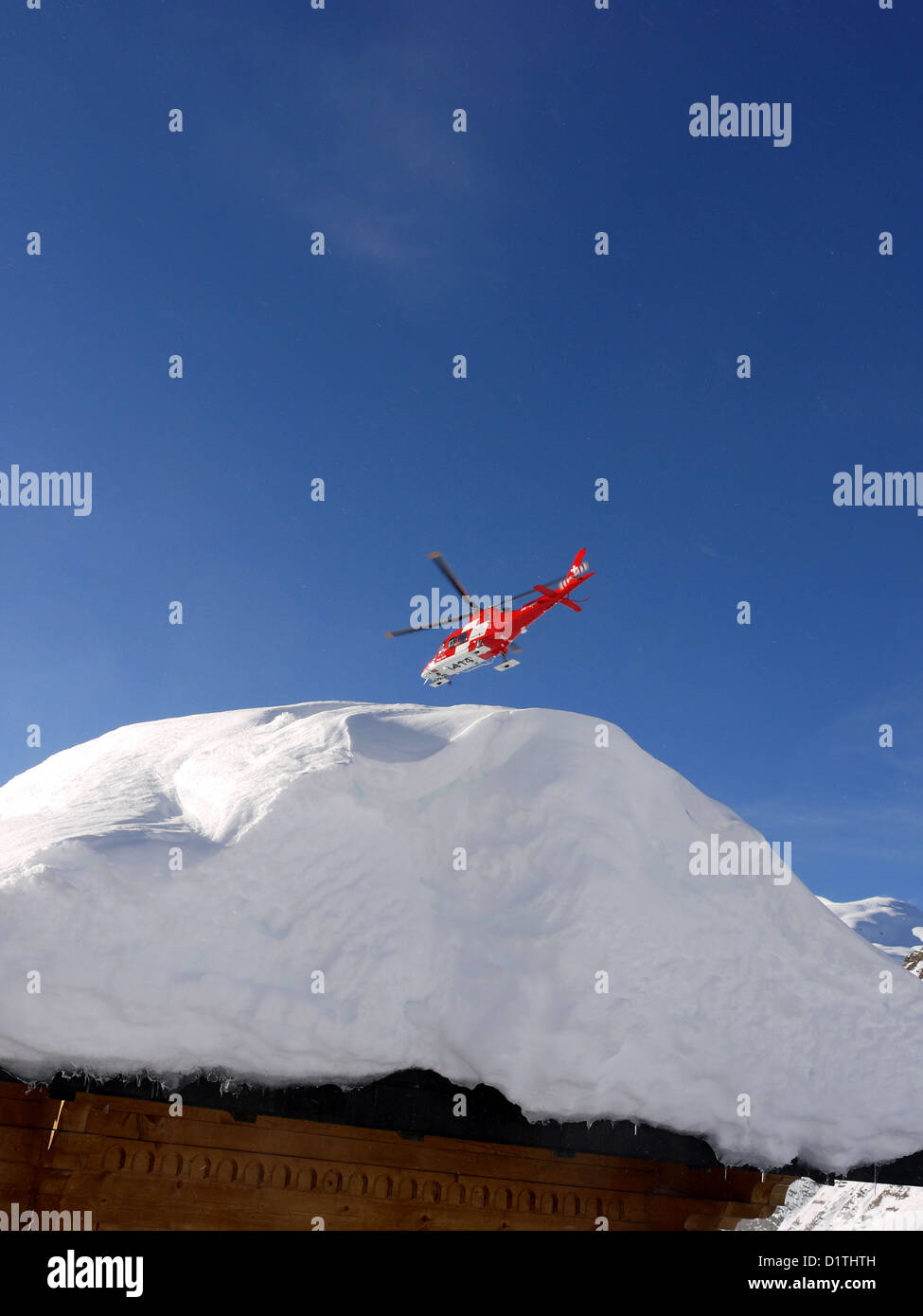 Rega Swiss mountain rescue helicopter flying over a chalet roof laden with snow Stock Photo