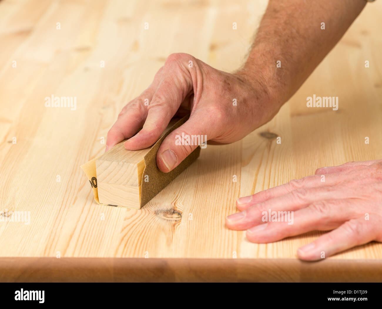 Man holding sanding block on pine floor or table sanding surface Stock Photo