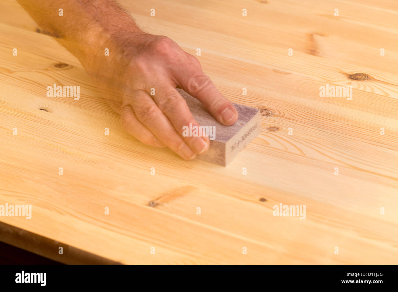 Man rubbing sanding block on pine floor or table with ghosting to suggest movement Stock Photo