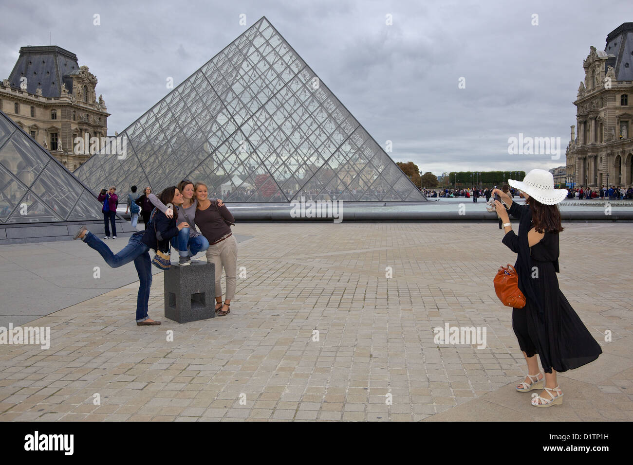 A young woman photographs  a group of friends in front of the Louvre glass pyramid, Paris, Ile de la Cite, France Stock Photo