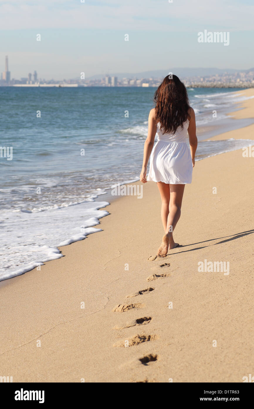 Beautiful woman walking on the beach with her footprints back Stock