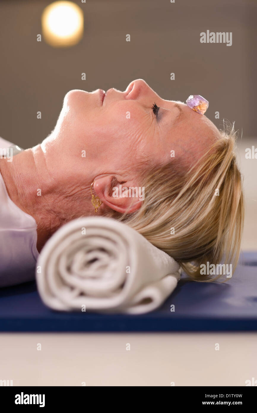 Senior woman relaxing and lying on pad with amethyst, quartz and other crystals on body. Side view Stock Photo