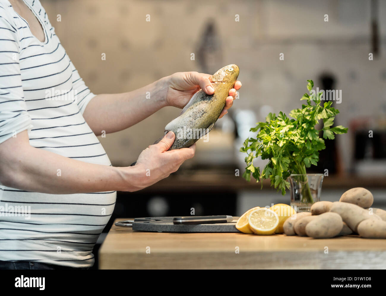 Pregnant woman, 35 years old, cooking fresh trout in a kitchen. Stock Photo