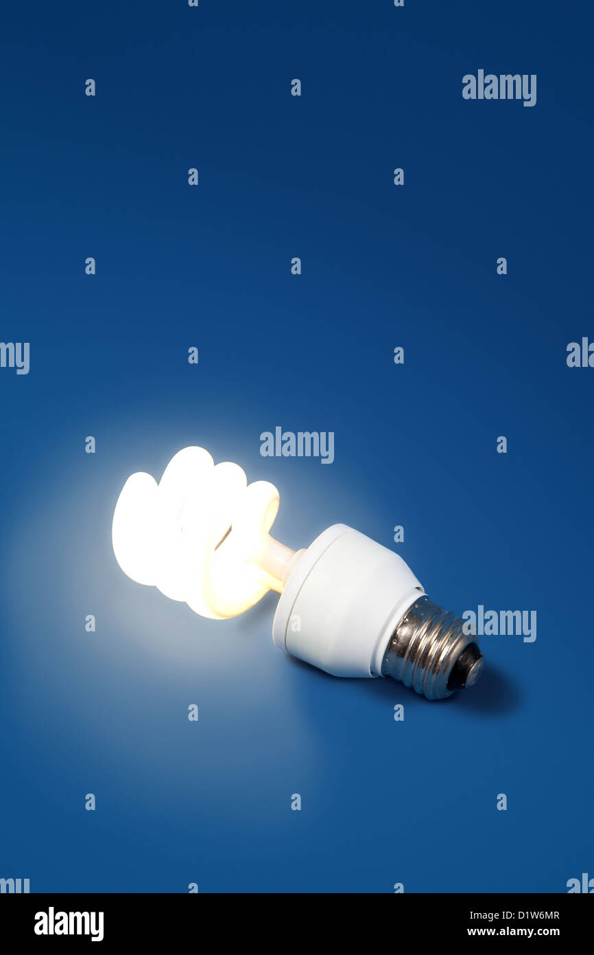 A low watt light bulb is lit up despite being unplugged and lying on it's side on a blue surface. Stock Photo