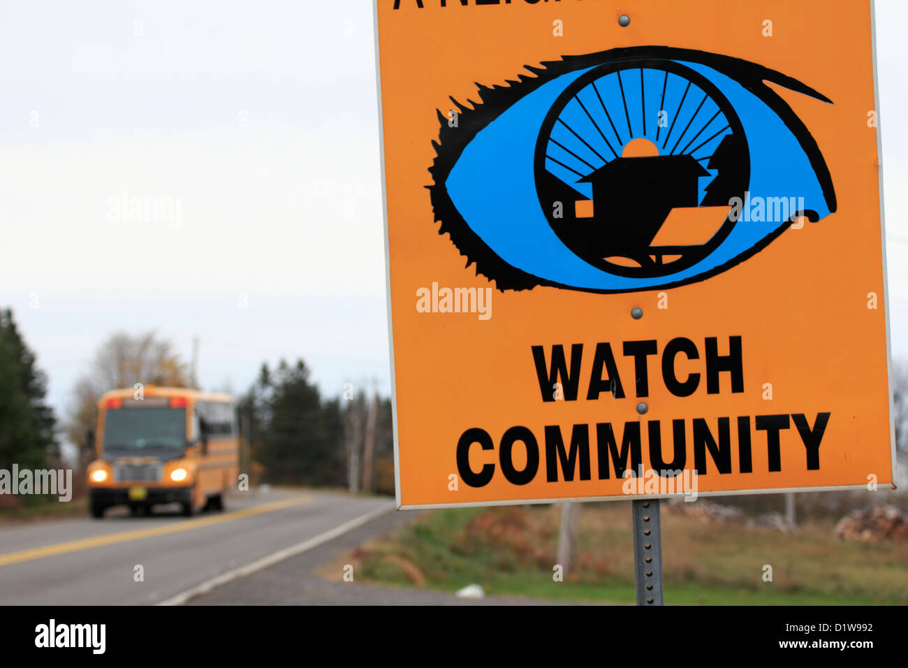 A school bus  passing a neighborhood watch sign beside a road Stock Photo