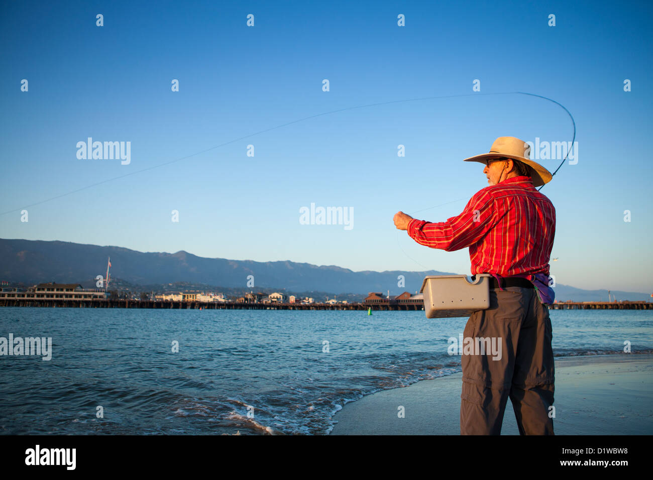 Saltwater flyfisherman casting for surf perch with the wharf in the background, harbor sandbar, Santa Barbara, California Stock Photo