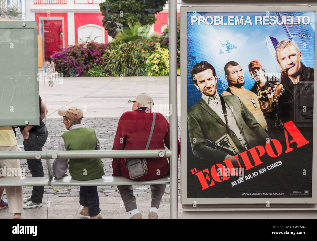 Two elderly Spanish men next to El Equipo A (The A Team in Spanish) film poster at bus stop in Spain Stock Photo