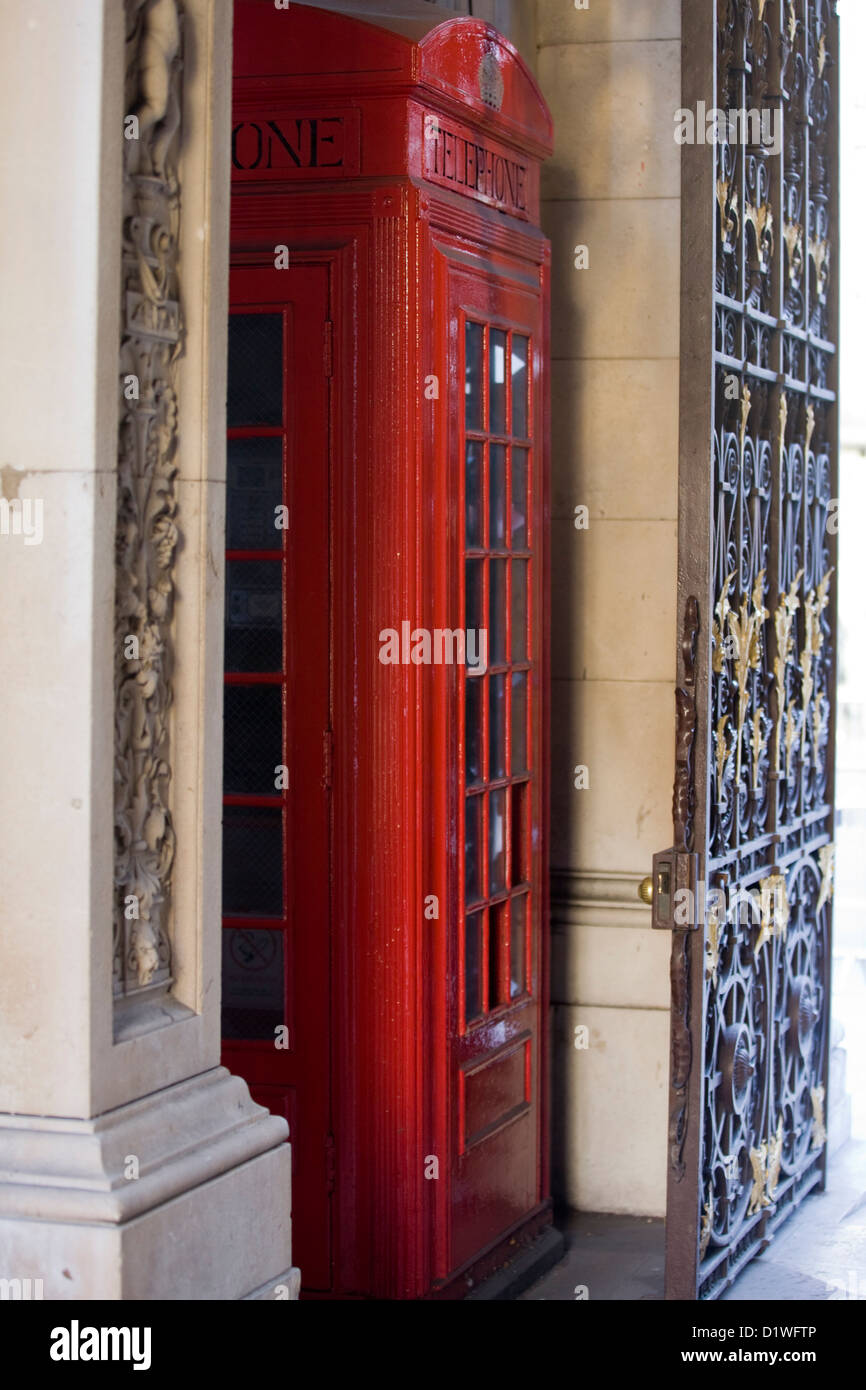 Red Telephone Box Sandwiched between a Iron Gate and a Wall Stock Photo