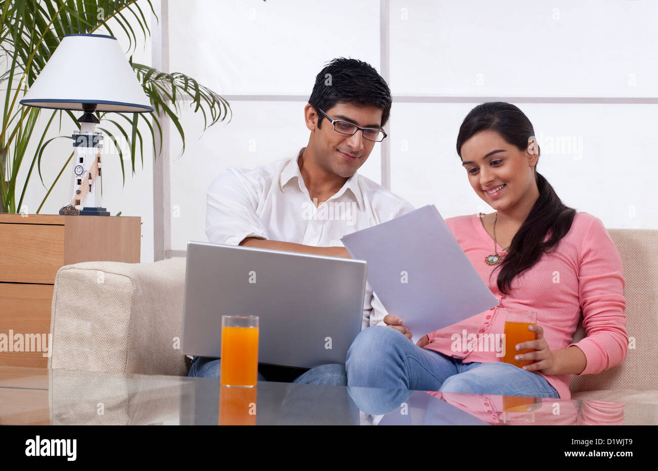 Young couple sitting on sofa using laptop while reading document Stock ...