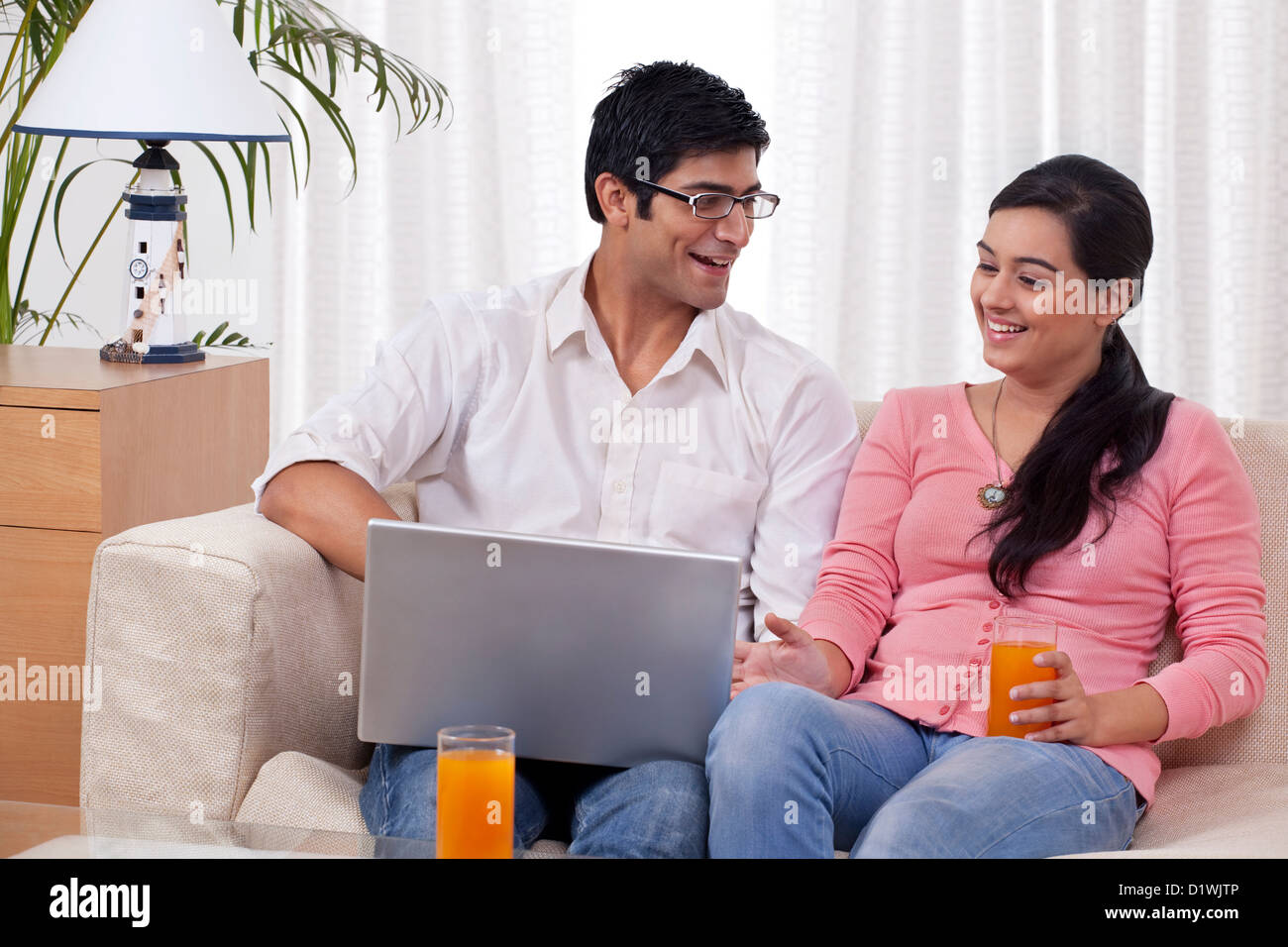 Young couple sitting on sofa using laptop with juice Stock Photo - Alamy