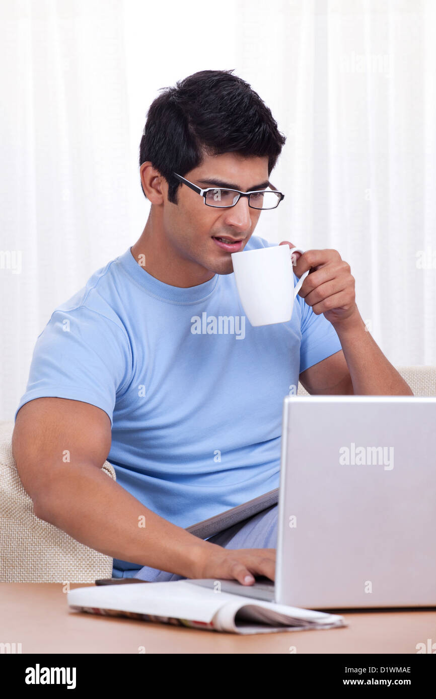 Young man taking a sip of coffee while operating laptop Stock Photo