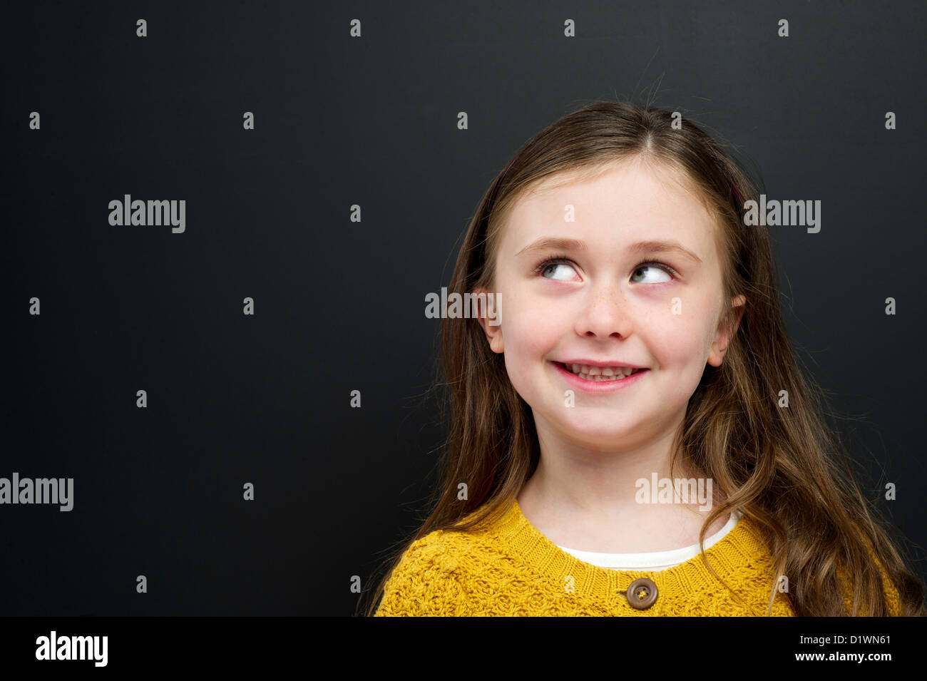 Smart young girl wearing a yellow jumper stood in front of a blackboard