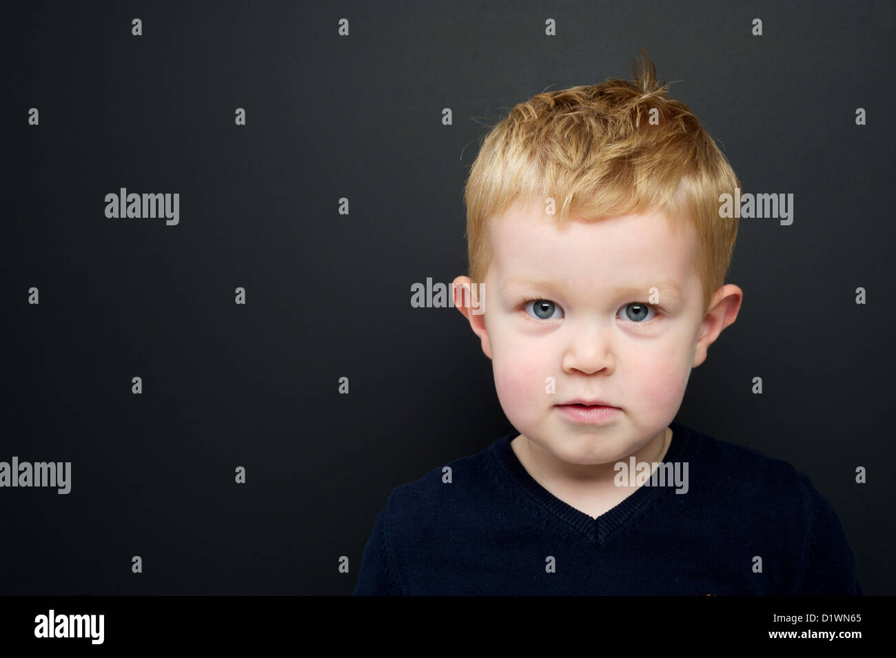 Smart young boy wearing a navy blue jumper stood in front of a blackboard Stock Photo