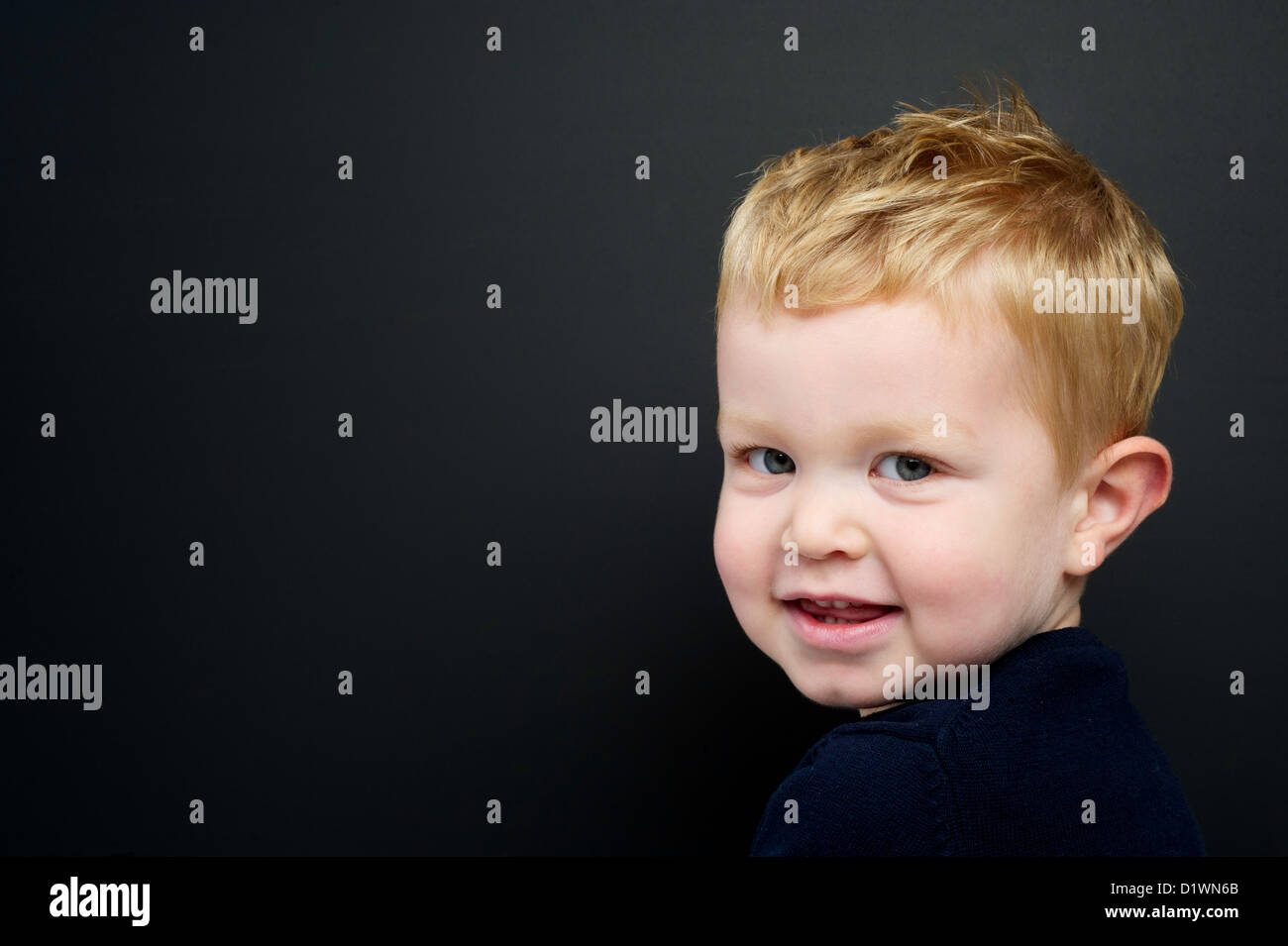 Smart young boy wearing a navy blue jumper standing in front of a blackboard Stock Photo