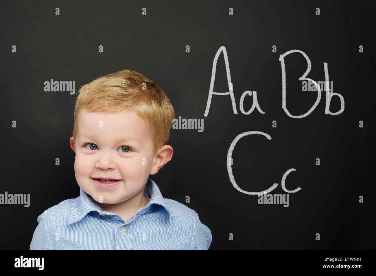 Smart young boy wearing a blue striped shirt standing in front of a blackboard Stock Photo