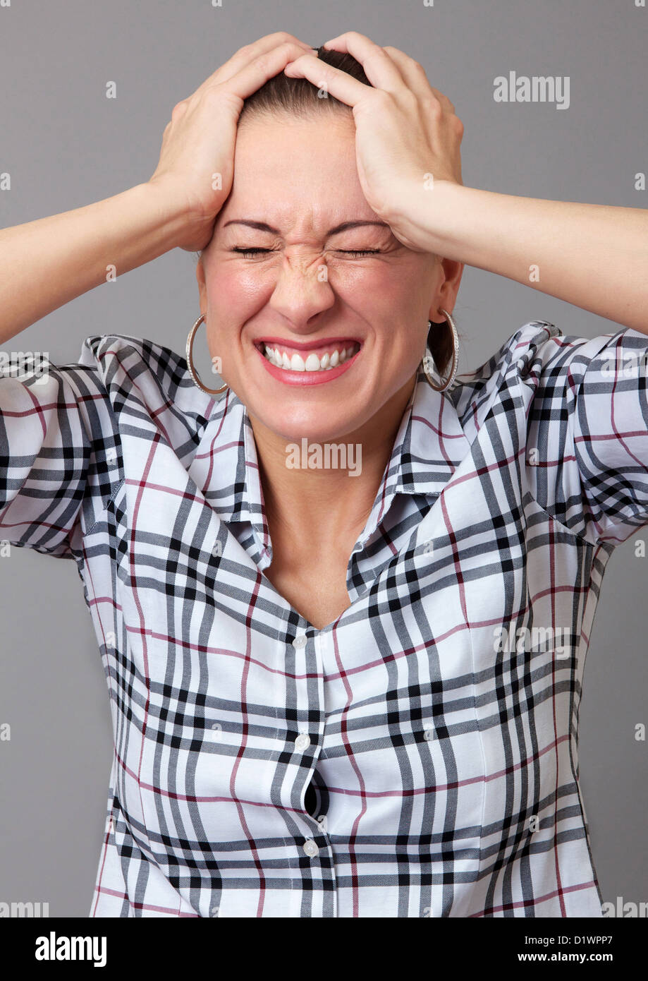 Woman with a pained expression on her face and her hands on her head ...