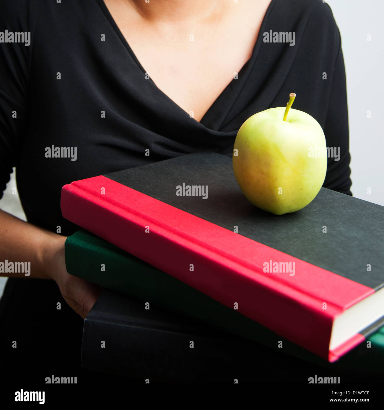 Woman holding text books with apple on top, arms and chest area shown only Stock Photo