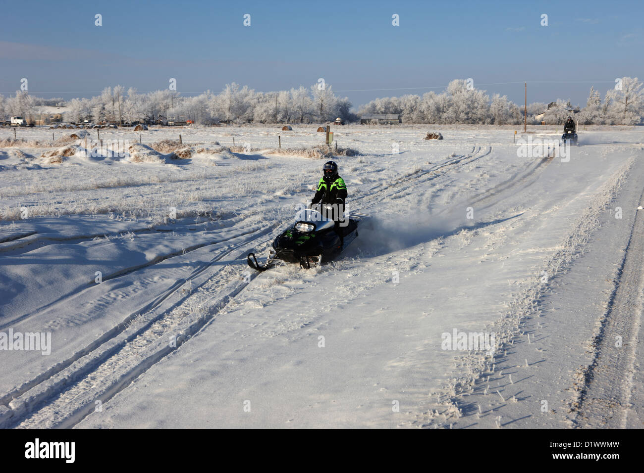 two men on snowmobiles crossing frozen fields in rural Forget Saskatchewan Canada Stock Photo