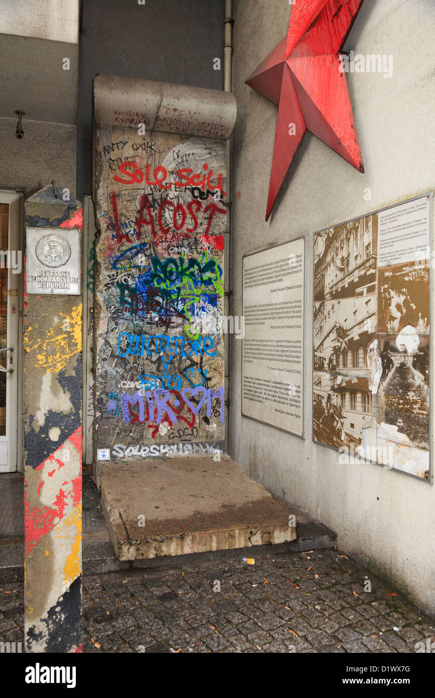 Graffiti on a section of original wall with information, red star and a GDR border post outside Checkpoint Charlie Museum Stock Photo