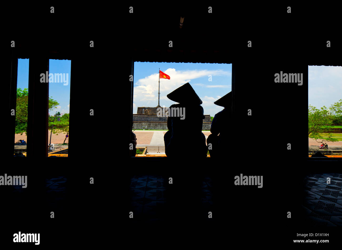 Women with conical hat sitting in front of Flag tower as Seen from the Forbidden Purple City, Hue, Vietnam Stock Photo