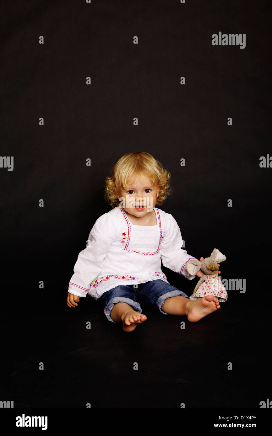 Two year old blonde infant girl in white shirt and denim on black background Stock Photo