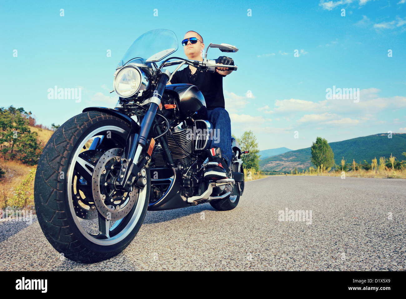 Young biker posing on a customized motorcycle on an open road Stock Photo